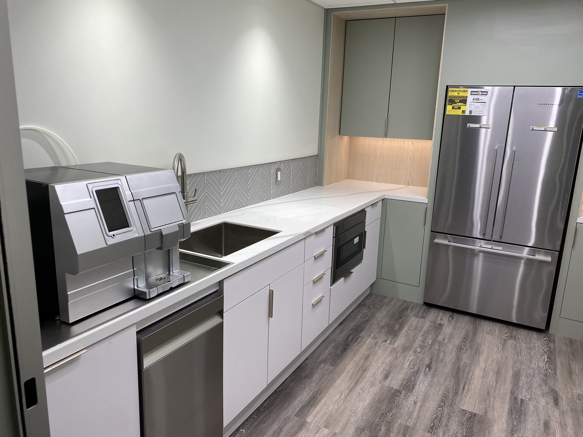 Breakroom with white slab-front lower cabinets, sage green tall storage, and a white veined countertop