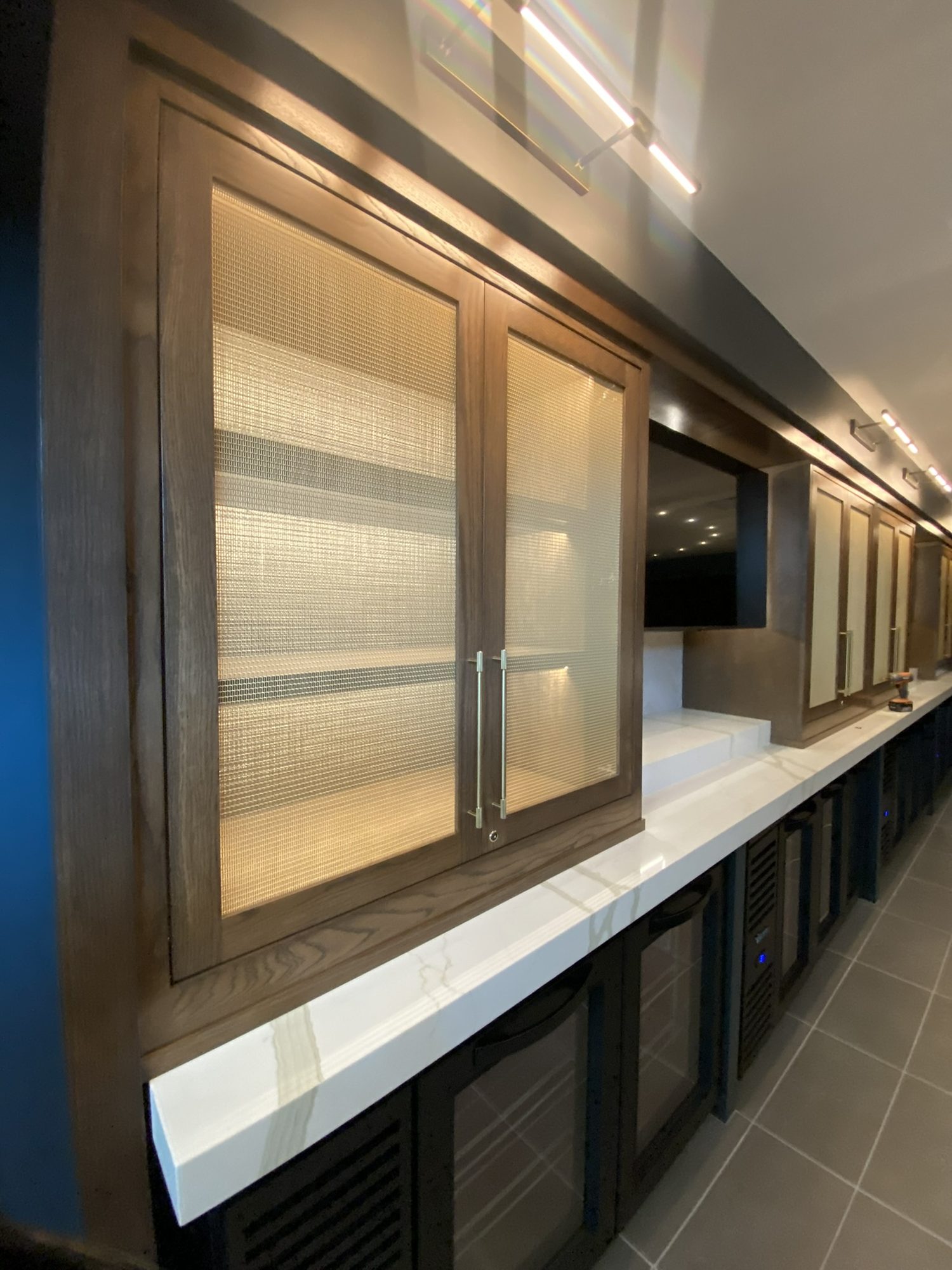 Back bar with stained oak cabinetry, woven mesh insert doors, and a white veined countertop over undercounter refrigeration